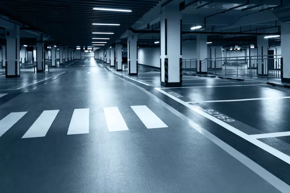 Black and white tinted photo of underground parking garage with black floor, white crosswalk, and harsh lighting.